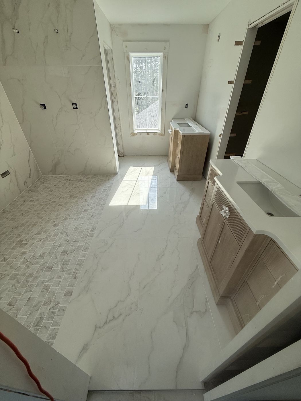 Master bathroom with large marble-look floor tile and a herringbone mosaic strip