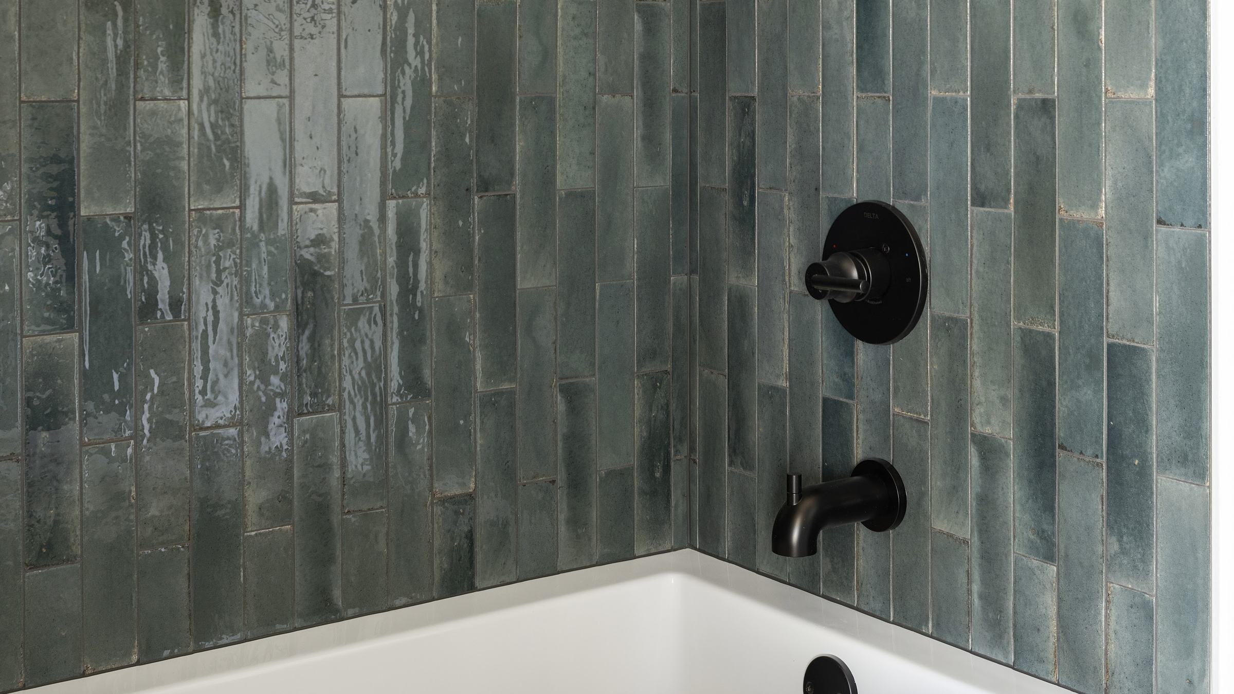 Tub surround in deep teal glossy vertical tile with a long niche