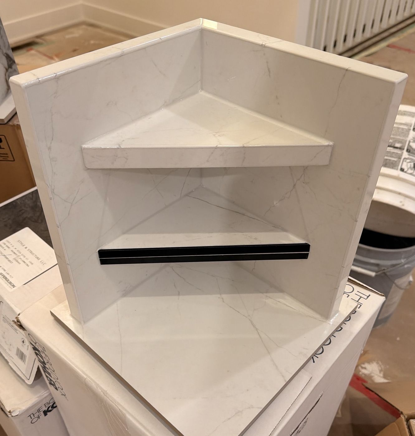 Corner shower shelf built from marble-look tile with crisp mitered edges