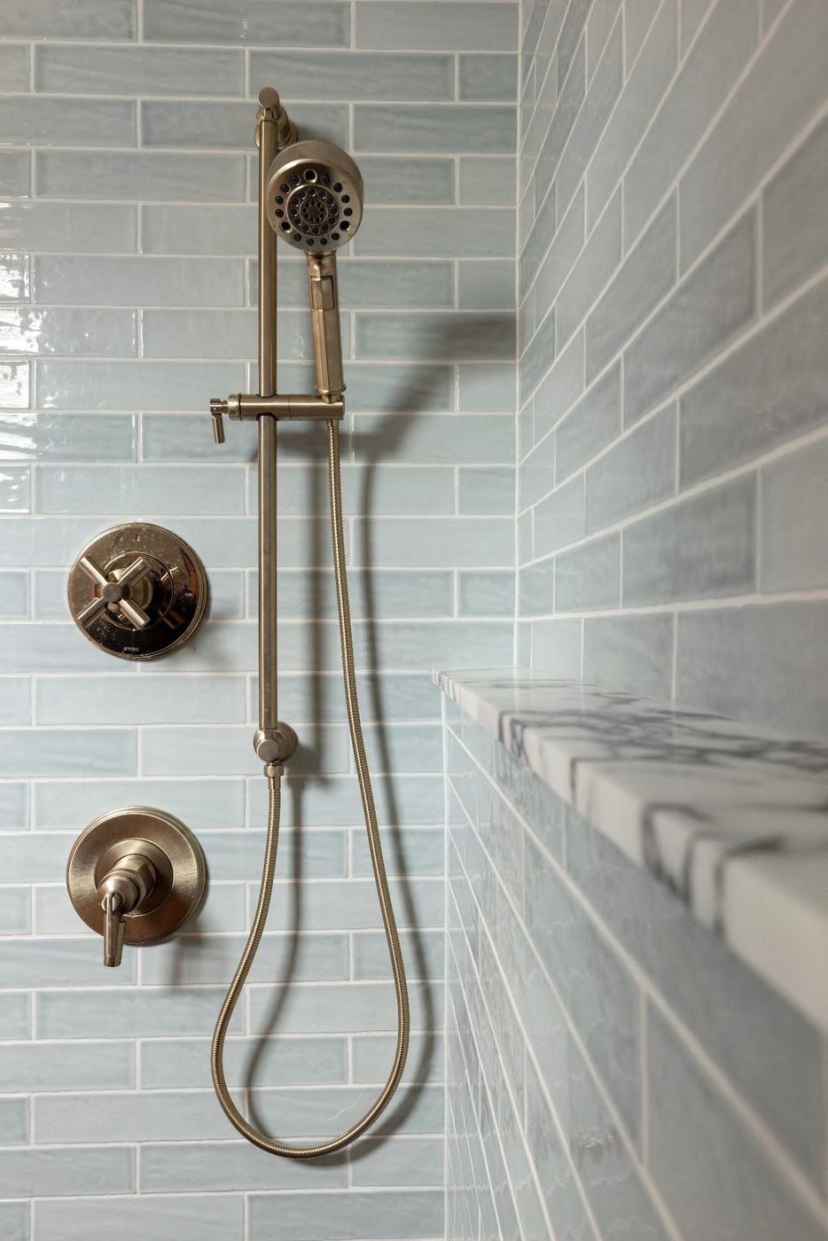 Pale blue glossy subway tile shower with a marble ledge