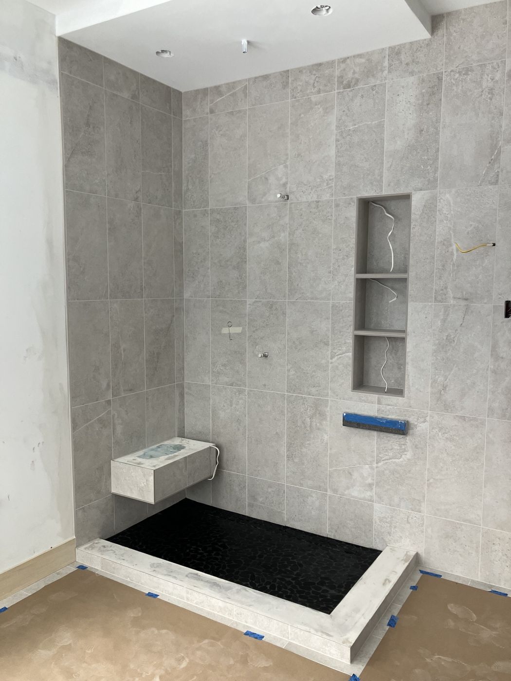 Large gray tile shower with a tall three-shelf niche and a floating bench
