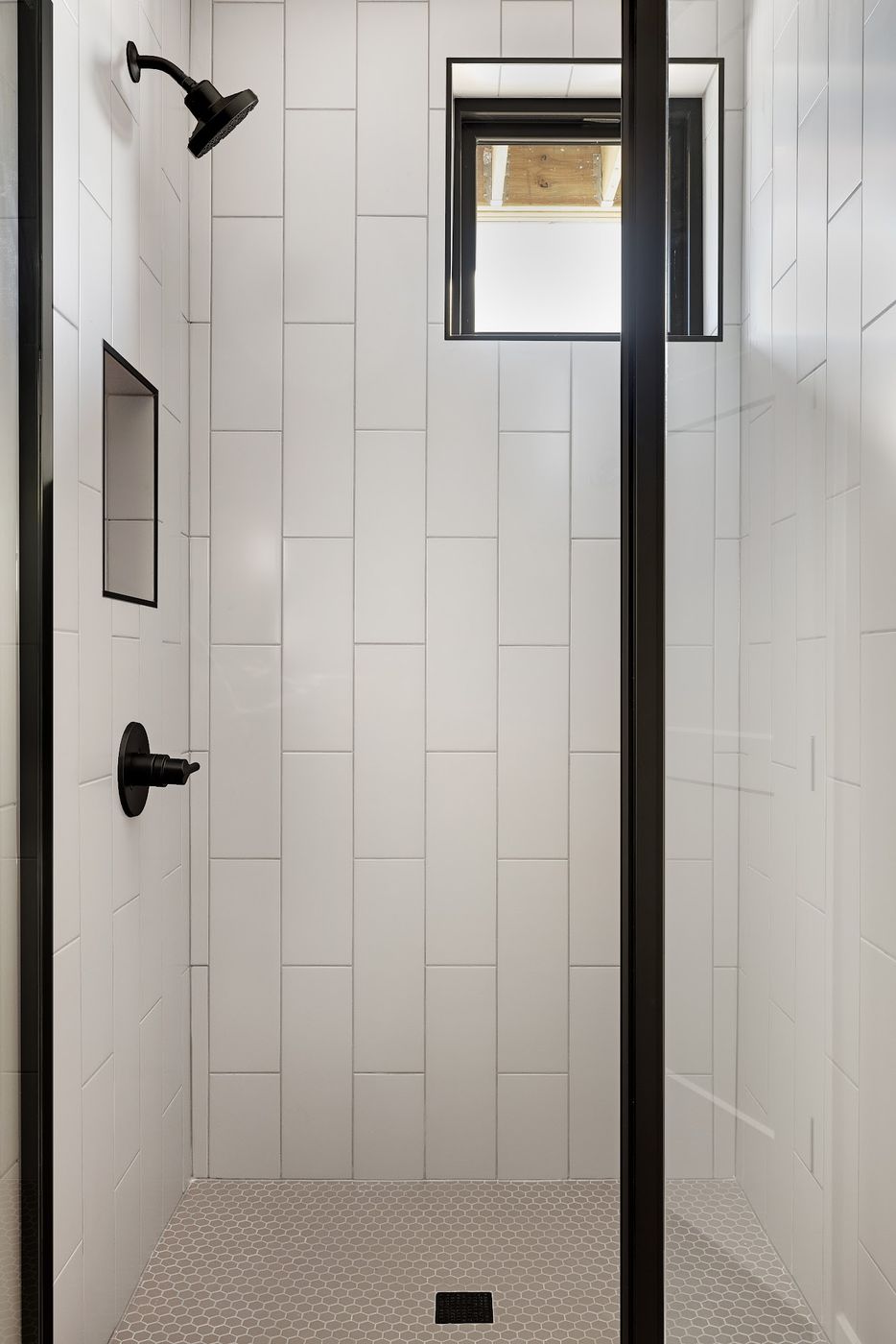 Shower with white tile laid vertically, a niche and a window